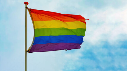 LGBT background - Rainbow flag waving on blue sky with clouds