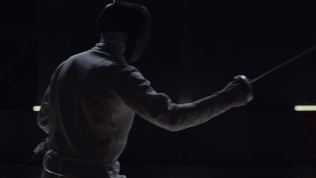 Two professional male fencers having a sabre fight in against dark background