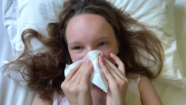 girls have a runny nose she blows her nose a white napkin she has either a cold or a seasonal allergy she lies on the pillow her hair is loose white bed. High quality 4k footage