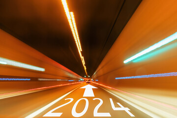 2024 text and arrow forward written on the asphalt road in tunnel with blurred light. Travel...