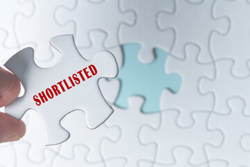 Hand holding piece of jigsaw puzzle with word Shortlisted.