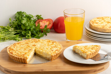 Cheese quiche, a pie on a wooden board, a slice of the pie on a white plate