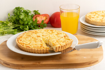 Cheese quiche, a pie on a wooden board, a slice of the pie being taken out