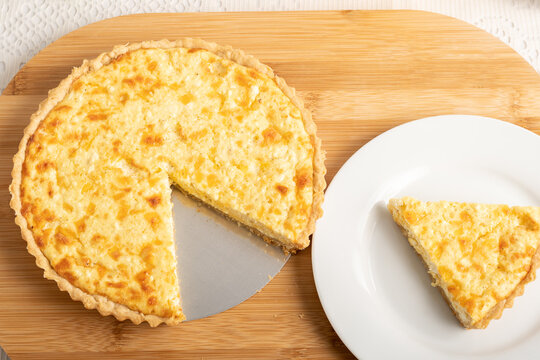 Cheese quiche, a pie on a wooden board, a slice of the pie on a white plate