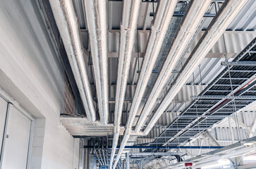 Metal pipes mounted under the ceiling are covered with thermal insulation at a modern production...