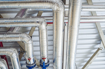 Metal pipes mounted under the ceiling are covered with thermal insulation at a modern production...