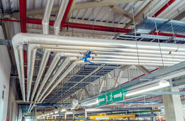 Metal pipes mounted under the ceiling are covered with thermal insulation at a modern production...