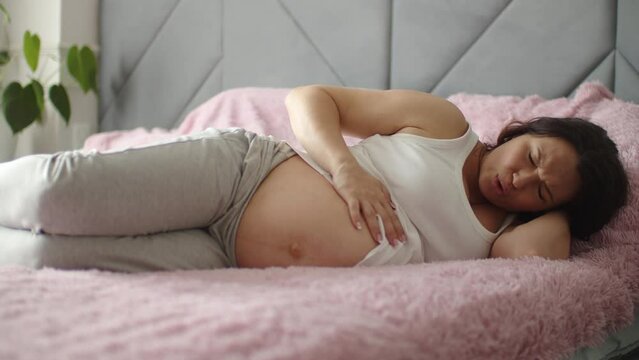 Expectant mother suffering from pregnant pain. Pregnant woman feeling ache lying on a bad.  Pregnant adult woman feels pain  expecting childbirth. Pregnant woman cannot fall asleep from abdominal pain