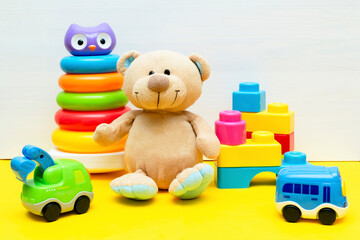 teddy bear with colorful constructor, pyramid, toy blocks, cars for children play on white yellow background, baby's childhood development, Educational logic toys for toddler kid's concept