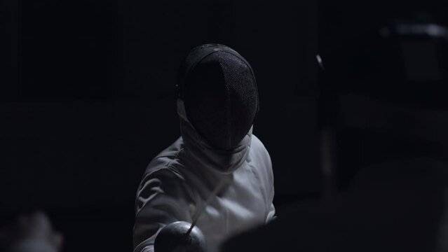 Two professional male fencers having a sabre fight in against dark background