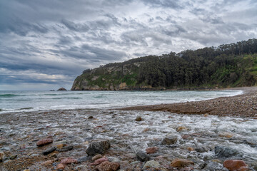 river flows into the ocean at a rocky beach in a small picturesque bay under an expressive sky