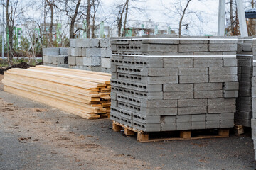 Concrete blocks are stacked in even rows, a warehouse of building materials in the open air, boards lie in a heap on the ground, flat bricks for building a house.