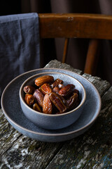 dates in a gray bowl on a wooden table, the back of a chair is visible from behind the table