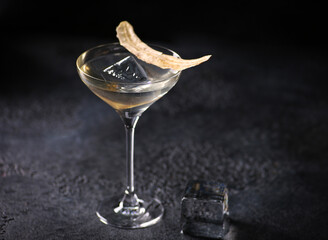 Drinks and beverages. A light cocktail in a transparent glass with banana chips and ice cube on black table. Restaurant, bar. Background image, copy space