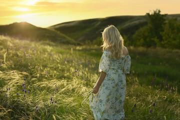 A woman in a spring summer field at sunset picking flowers into a bouquet.