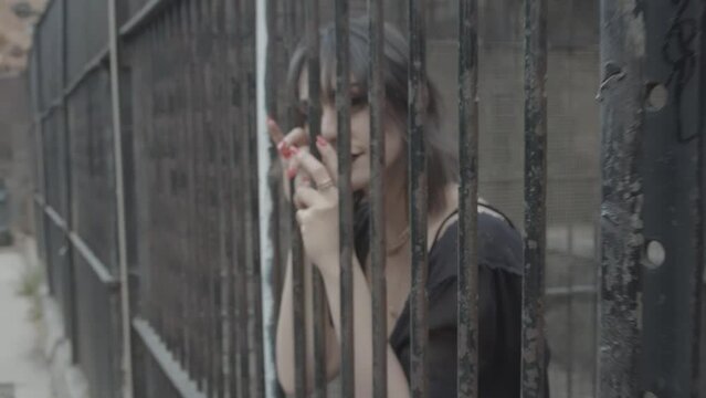 Beautiful girl with dark make-up and in a black dress locked in a cage, where she holds a lattice and smiles into the camera