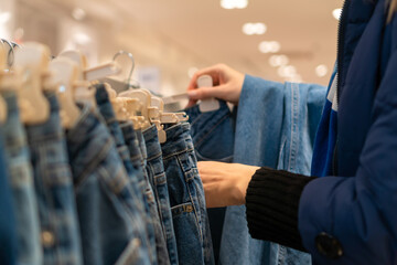 Close-up of women's hands choosing blue jeans at the mall. Shopping concept