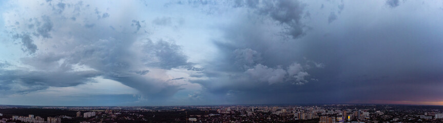 Aerial evening wide panoramic view on city with dramatic heavy cloudscape, sky with clouds. Evening flight above city streets. Kharkiv, Ukraine city center park and residential district