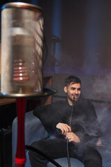 young smiling man with a hookah pipe in his mouth. hookah with a protective screen in the foreground