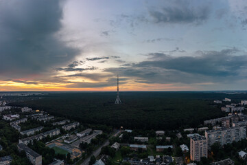 Obraz premium Aerial panoramic sunset evening city view on telecommunication tower antenna in forest near residential district and scenic cloudy sky. Kharkiv, Ukraine