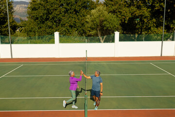 High angle view of biracial senior couple giving high-five while playing tennis in court in summer
