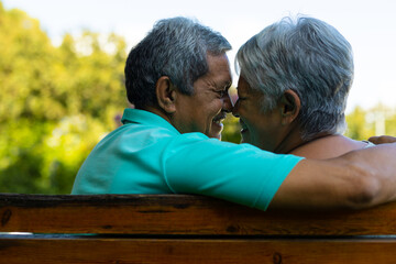 Close-up of smiling biracial senior couple looking at each other while sitting on bench in park
