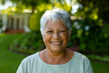 Close-up portrait of smiling biracial senior woman with short gray hair against trees in park - obrazy, fototapety, plakaty