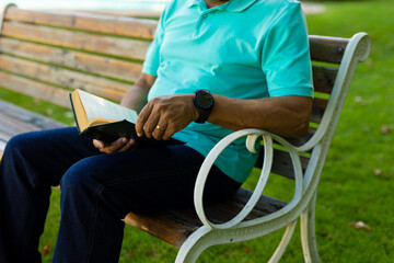 Obraz premium Midsection of biracial senior man wearing watch reading book while sitting on wooden bench in park
