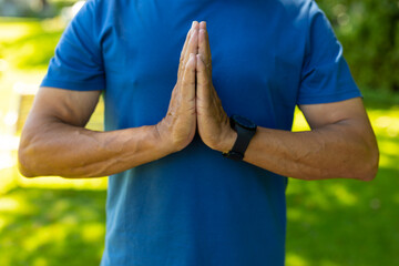 Midsection of biracial senior man wearing blue sports clothing standing in prayer position at yard