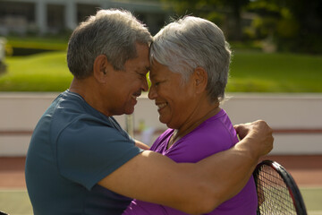 Close-up of happy biracial senior couple with eyes closed and face to face romancing at tennis court