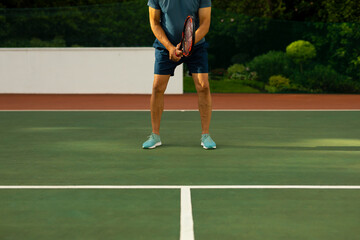 Low section of biracial senior man wearing sports clothing and shoes holding racket on tennis court - Powered by Adobe