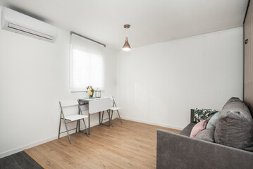 Studio apartment with metal and white madra folding two-seater dining table with matching chairs under sheer blind windo
