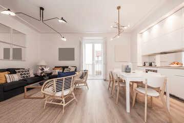 Living room with open kitchen with white furniture, dining table with matching wooden chairs, wicker armchairs and sofas upholstered in blue fabric