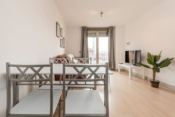 Living room with a small square dining table with a white marble top, gray metal chairs and a flat-screen TV on a white sideboard and a balcony with white wood and glass doors