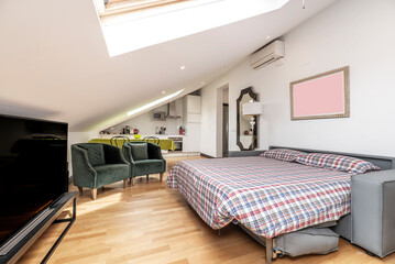 Apartment with sloping ceilings, unfolded sofa bed with checkered duvet, wooden floors and large skylights in the ceiling