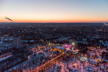 Aerial view on evening city lights, streets, Ferris wheel, entertainments in winter, covered in...