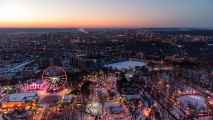 Aerial panorama on vivid evening cityscape, Ferris wheel and entertainments in winter, covered in white snow. Kharkiv city center in sunset colors, amusement Gorky Central Park