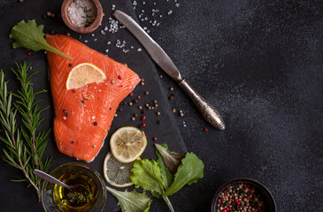 Uncooked raw salmon fish with herbs on dark background