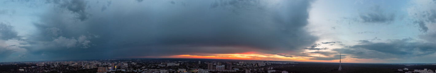 Dramatic ultra wide sunset cloudscape panorama view in city residential district. Aerial Pavlovo Pole, Kharkiv Ukraine. Evening skyscape, cloudscape with heavy dark clouds and orange sun