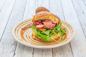Sandwich with brioche muffin, pastrami slices, lettuce sprouts, pickled cucumber, radish slices and...