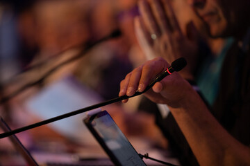 Pendant une conférence ou séminaire, une main tient un micro pendant un discours. Le discours est écrit sur une tablette ou un ordinateur portable.