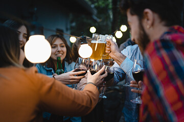 a lively group of friends toasting in the terrace of the restaurant pub in the countryside under the lights outdoors - concept of people having fun drinking and eating together on summer weekends