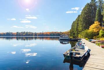 Small boats tied up to a wooden jetty on a beutiful lake surronded by a deciduous forest on a sunny autumn day. Lens flare and autumn colours.