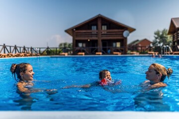 Mom plays with her daughter and little son in oversleeves in the pool on summer vacation