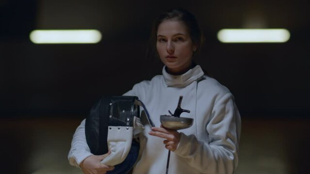 Portrait of female fencer taking off her helmet, posing and looking into camera