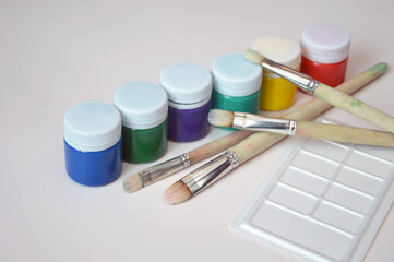 Multi-colored gouache paint in closed jars and a set of artistic brushes. Drawing materials,...