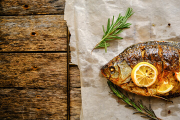 Baked fish cooked on parchment paper with spices, lemon and rosemary on a wooden background.