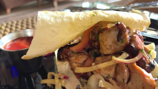 hot kebab on a black plate in a restaurant with lettuce and tomatoes steak lies on a thin pita bread and looks very appetizing. High quality 4k footage