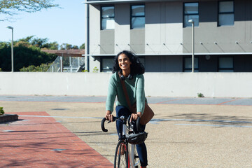 Happy young biracial businesswoman commuting through bicycle in city on sunny day - Powered by Adobe