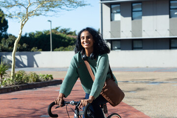 Portrait of happy young biracial female advisor riding bike while commuting in city on sunny day - Powered by Adobe